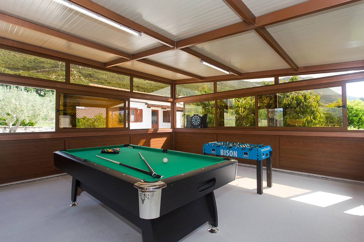 Same enclosed outdoor wooden space, viewed from a different angle, featuring a dartboard, foosball table, and billiards.